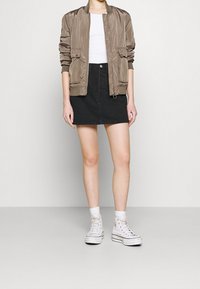 Khaki bomber bunda s žebrovanými manžetami, bílým tričkem, černou denimovou sukní a bílými vysokými teniskami. Jednoduchý design, neformální styl.