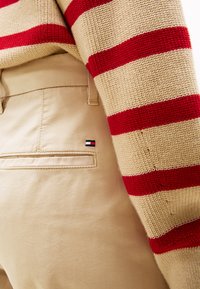 Crème en rode gestreepte gebreide trui gecombineerd met beige broek met een klein geborduurd logo detail nabij de achterzak.
