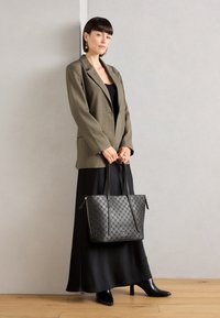 Sac fourre-tout noir à motif avec une texture en cuir lisse, des poignées doubles et une fermeture zip, associé à un blazer olive et une longue robe noire.