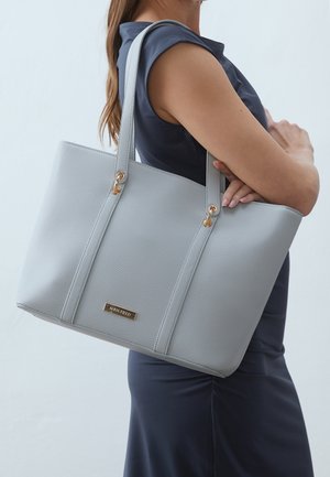 Sac fourre-tout en similicuir gris avec une finition texturée, des accents de quincaillerie dorée et des bretelles courtes, arborant une étiquette de marque à l'avant.