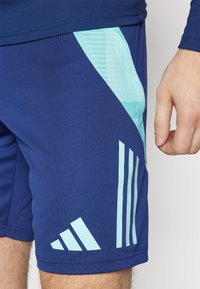 Pantalones cortos deportivos azul marino con acentos en azul claro, que presentan un patrón geométrico y tres rayas verticales en el lateral. Fabricados con tela texturizada.