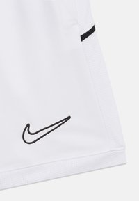 Λευκά αθλητικά σορτς με κεντημένο μαύρο λογότυπο Nike Swoosh κοντά στο τελείωμα και μαύρη λεπτομέρεια περιθωρίου στο πλευρικό πλέγμα.