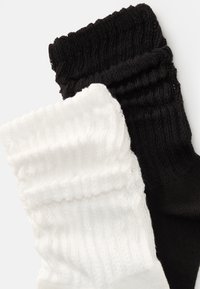 Divi saspringti zeķu pāri: viens balts un viens melns, izgatavoti no mīksta, adīta auduma ar ribotu tekstūru un elastīgiem galiem.