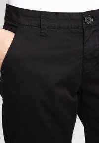 Pantalon noir en tissu lisse avec un design classique. Présente une poche avant, un bouton de fermeture et des détails de couture subtils.