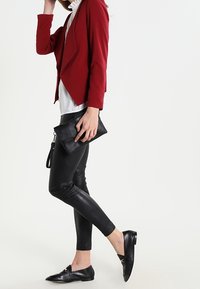 Blazer rosso su misura, camicia bianca, pantaloni in ecopelle neri con accenti testurizzati, ballerine nere e una clutch nera. Design minimalista.