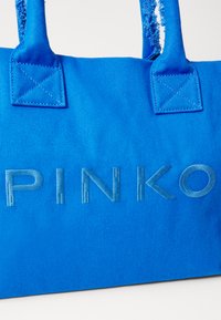 Sininen kankainen olkalaukku, jossa on kohokuvioitu "PINKO"-kirjotus, tukevat kahvat ja teksturoitu pinta. Koristeina on ristipistot kahvan alaosissa.
