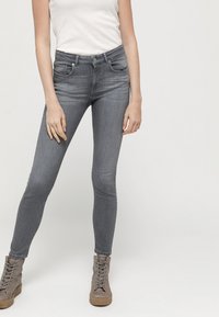 Vaqueros ajustados grises con una cintura de media altura, bolsillos frontales y una textura de denim suave. Combinados con botas de tobillo grises con cordones.