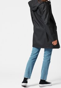 Svart vattentät jacka med huva, med tryckknappar och en något avslappnad passform, kombinerad med ljusblå jeans och svarta sneakers.