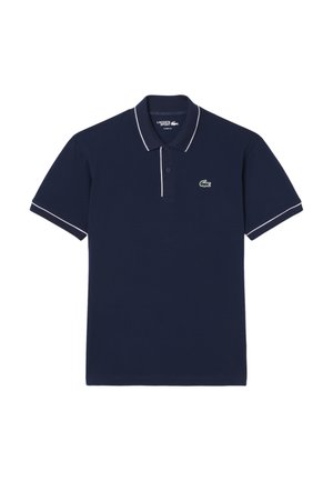 Polo de algodón azul marino, con cuello y ribetes en las mangas blancos en contraste, y un logo de cocodrilo verde en el pecho.