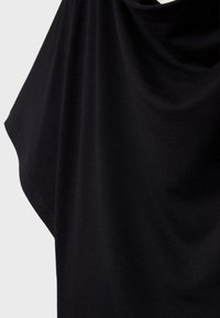 Čierna tkanina jemne padá, vyznačuje sa hladkou štruktúrou s jemnými záhybmi a mäkkými krivkami, vytvárajúc plynulú siluetu.