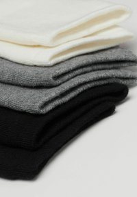 Ensemble de quatre paires de chaussettes repliées en blanc, gris clair, gris foncé et noir. Fabriquées en tissu doux et texturé avec des bords côtelés.