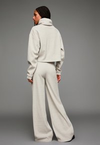 Ljusgrå, stickad koordinerad set som består av en kortärmad polotröja och vida byxor. Tillverkad av mjukt, strukturerat material.