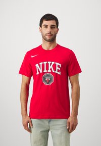 Punane puuvillane T-särk, millel on suur valge "NIKE" logo ja Chicago Bullsi embleem musta äärisega. Lühikesed varrukad, ümmargune kaelus.
