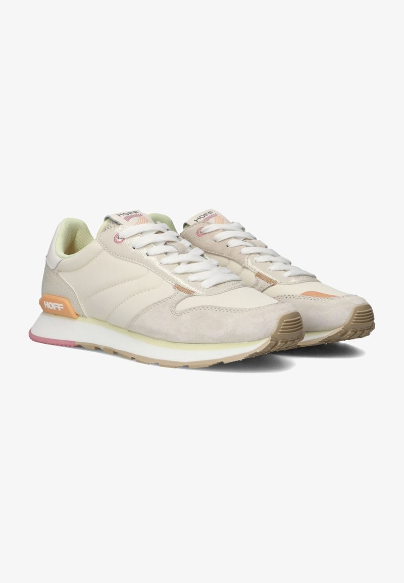 Zapatillas con una parte superior sintética beige, acentos de ante claros, cordones blancos y una suela de goma que presenta un detalle en el talón en color rosa y naranja.