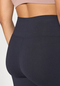 Högmidjade leggings i ribbad mörkblått tyg med jämn textur och enkel söm längs midjan.