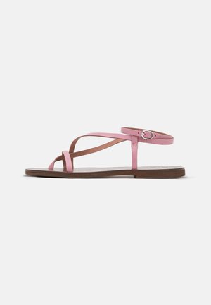 Platte sandaal met bruine zool en dunne roze bandjes die over de tenen en enkel kruisen, met een kleine ronde zilveren gesp aan de zijkant.