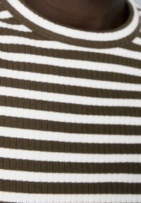 Haut en maille côtelée à rayures horizontales marron foncé et blanches. Vue rapprochée de l'encolure et de la texture du tissu.