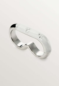 Anillo de metal plateado con un diseño ondulado acentuado por una parte superior suave y translúcida que presenta dos pequeñas protuberancias elevadas.