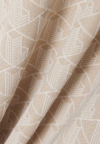 Tessuto beige intrecciato con motivo geometrico bianco. La trama è liscia con una sottile lucentezza, che mette in risalto linee e curve.