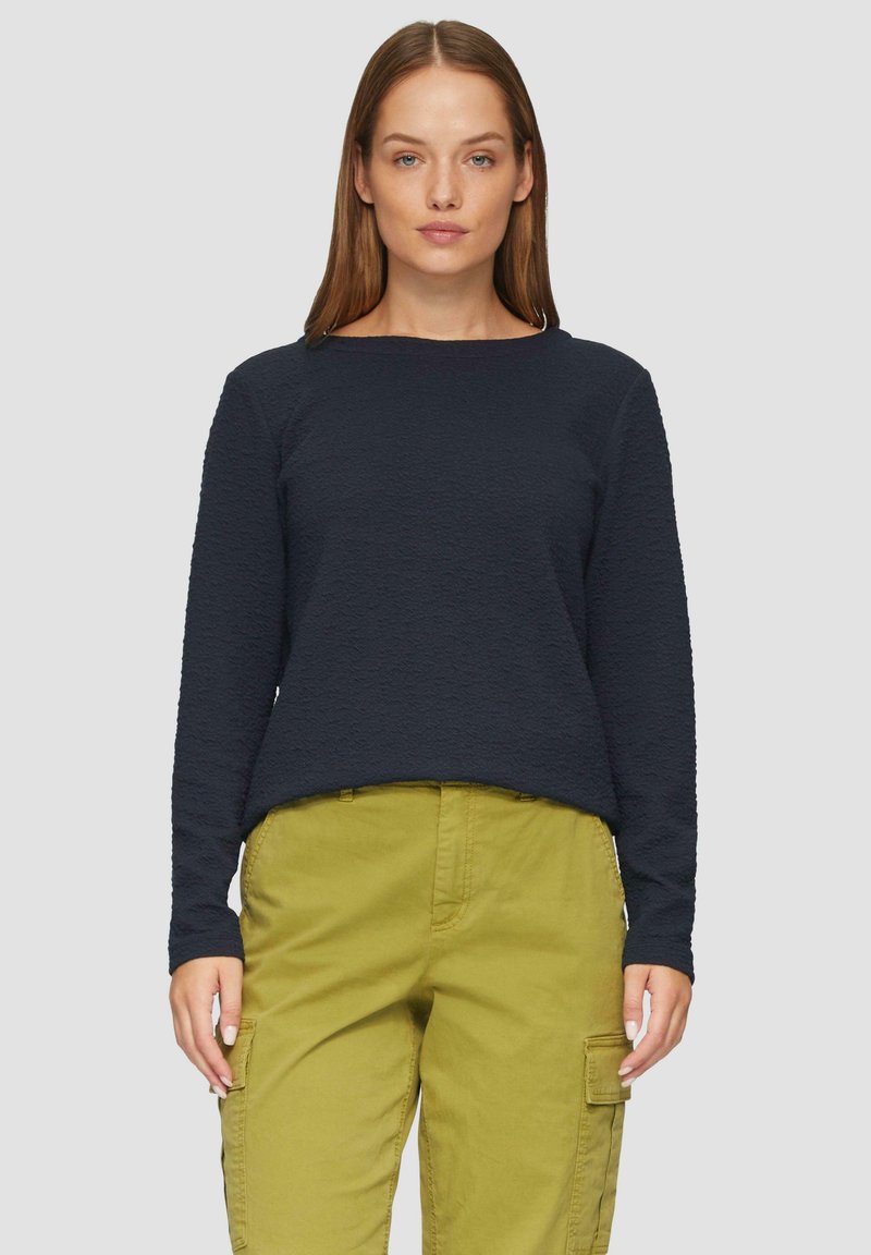 Marineblauwe pullover van textuurstof, met ronde hals en lange mouwen, gecombineerd met licht olijfgroene cargobroek met zakken.