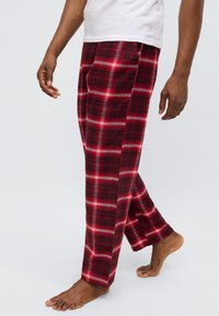 Κόκκινα παντελόνια φόρμας με καρό σχέδιο σε λευκές και μαύρες γραμμές, άνετη εφαρμογή, βαμβακερό υλικό, ίσια μπατζάκια, χωρίς εμφανή διακοσμητικά ή τσέπες.