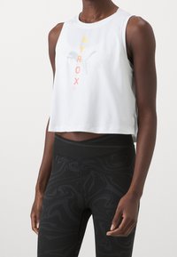 Valkoinen lyhyt toppi, jossa on värikäs "HYROX" -painatus, yhdistettynä mustiin legginsseihin, joissa on pyörteinen kuvio ja joustava vyötärö.