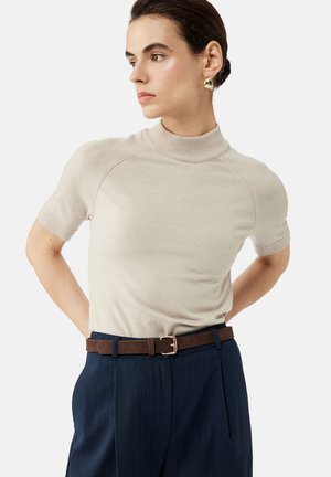 Top de punto suave de color beige con cuello alto simulando un cisne y mangas cortas, combinado con pantalones oscuros de rayas y un cinturón marrón con hebilla dorada.
