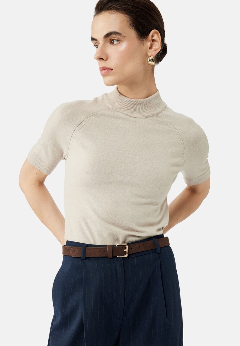 Top in maglina morbida beige a maniche corte con collo alla marinara, abbinato a pantaloni scuri a righe sottili e una cintura marrone con fibbia dorata.