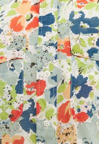 Blommig skjorta med knappar som har en ljusblå bakgrund med röda, orange och gröna blommor, samt två bröstfickor. Mjuk bomullstyg.