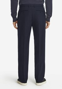 Granatowe spodnie o prostym kroju, z plisami z przodu, dwiema tylnymi kieszeniami i gładką teksturą. Noszone z ciemnym obuwiem.