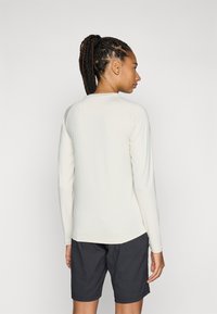Haut à manches longues crème avec un encolure arrondie, une coupe cintrée et des manches raglan, associé à un short sombre. Texture lisse, design épuré.