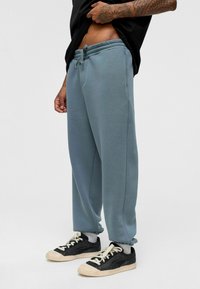 Lichtblauwe joggingbroek met een elastische tailleband en koord. Zachte textuur, taps toelopende enkelboorden, gestyled met zwarte sneakers.