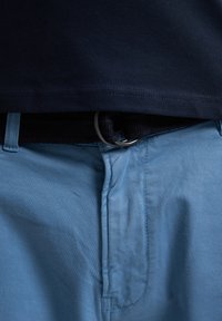 Polo tričko s krátkým rukávem v námořnické modři nad světle modrými kalhotami, s černým tkaným pásem a kovovou sponou. Hladká textura látky.