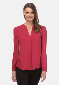 Langsleeve, diep rode blouse met knopen aan de voorkant, een V-halslijn en gathered schouderdetails; gladde textuur met een lichte glans.