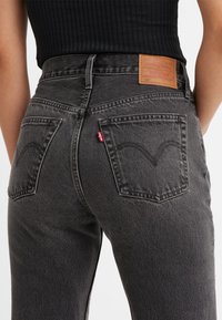 Jeans de mezclilla gris oscuro con un ajuste de tiro medio, que cuentan con una etiqueta de cuero en la parte posterior, costuras arcuadas en los bolsillos y una pequeña etiqueta roja.