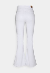 Jean blanc évasé taille haute avec poches arrière et un patch en cuir marron sur la ceinture, présenté de dos.