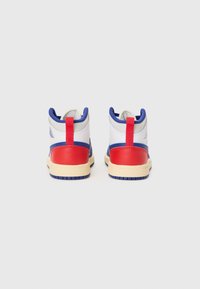 Baskets montantes avec une tige en cuir blanc, des accents rouges et bleus, une semelle beige et un onglet de talon rouge pour un enfilage facile.