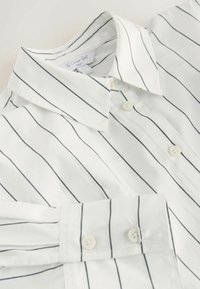 Chemise blanche à boutons avec fines rayures verticales noires, dotée d'un col classique et de boutons blancs. Tissu en coton doux et lisse.