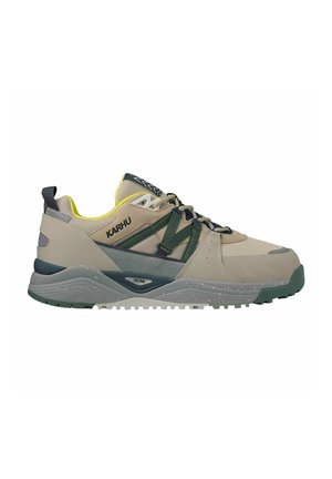 Chaussures de sport beiges et vertes avec un dessus texturé, un panneau en maille, un système de lacets distinctif et une semelle en caoutchouc mouchetée.