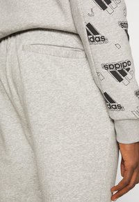 Sudaderas grises de tela suave, con un bolsillo y acentos impresos del logo negro "adidas" en la manga. Diseño clásico de jogger.