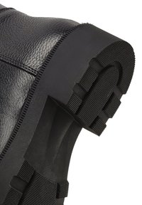 Schwarzer Lederschuh mit dicker Gummisohle, die ein tiefes, strukturiertes Profil für verbesserten Grip und Haltbarkeit aufweist.