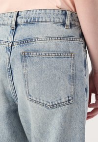 Lyseblå denimjeans med høy midje, rett ben og en enkelt baklomme med synlige sømdetaljer. Teksturert stoff.