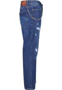Jean en denim bleu avec des pièces usées et une chaîne argentée attachée des passants de ceinture avant aux passants arrière, vu de côté.
