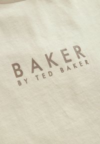 Beżowa tkanina bawełniana z wytłoczonym brązowym tekstem "BAKER BY TED BAKER." Powierzchnia jest gładka, z delikatnym połyskiem.