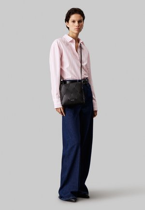 Kvinde iført en lyserød bluse med striber, mørke vidde jeans, sorte sko og en sort crossbody taske med quiltet mønster.