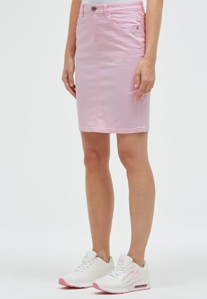 Frau trägt einen knielangen rosa Jeansrock mit Fronttaschen und weißen Sneakers mit pinken Akzenten auf weißem Hintergrund.