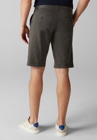 Shorts gris foncé en tissu léger, avec une texture lisse, deux poches arrière avec fermetures à boutons et un ourlet roulé.