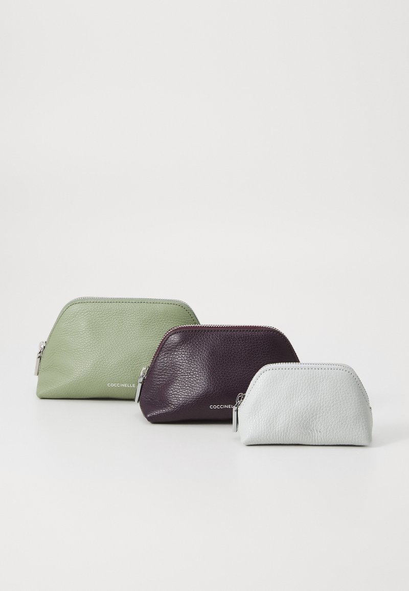 Três bolsas com zíper em couro texturizado nas cores verde claro, roxo escuro e cinza claro, de tamanhos variáveis, com um logotipo da marca discreto na parte da frente.