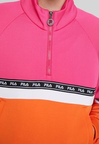 Close-up of pink and orange quarter-zip sweatshirt with white stripe and black FILA logo band across the chest.