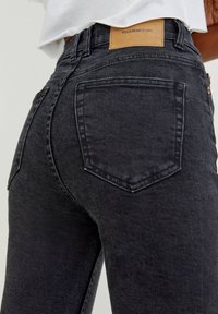 Jeans de denim negros con un diseño ajustado. Las características incluyen dos bolsillos traseros, una etiqueta de cuero en la cintura y una textura suave.